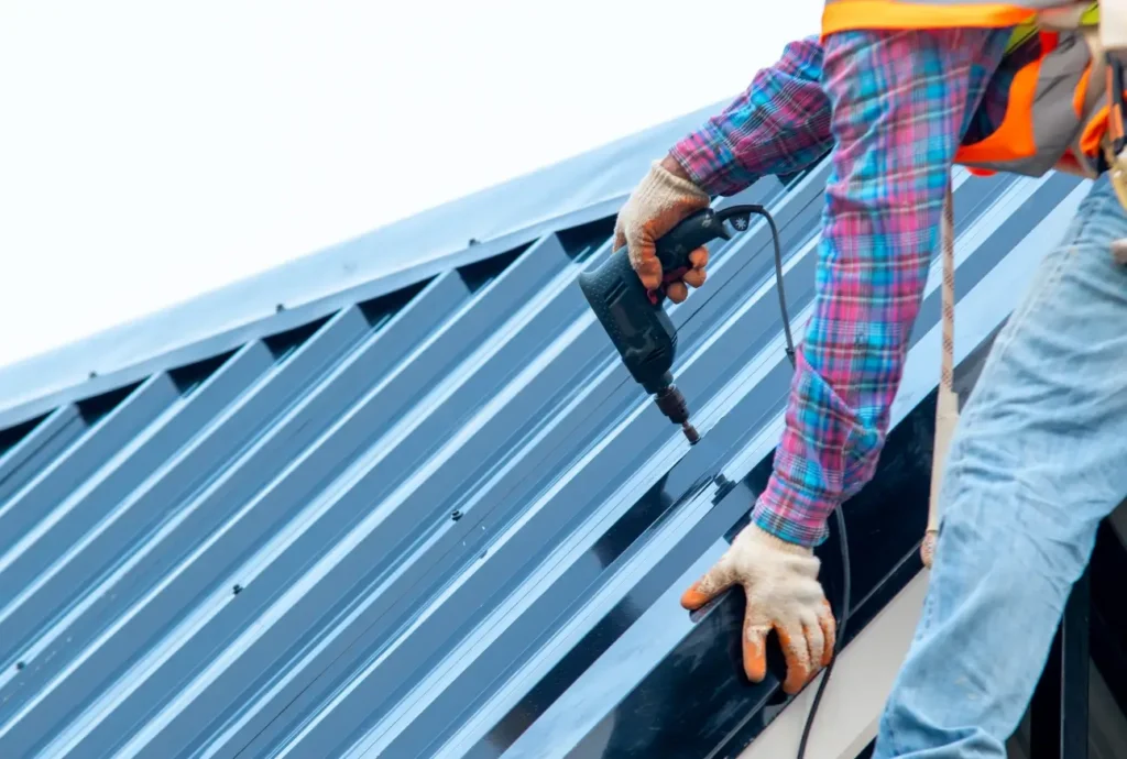 Close-up of a roofer using a power drill to install dark blue corrugated metal roofing panels
